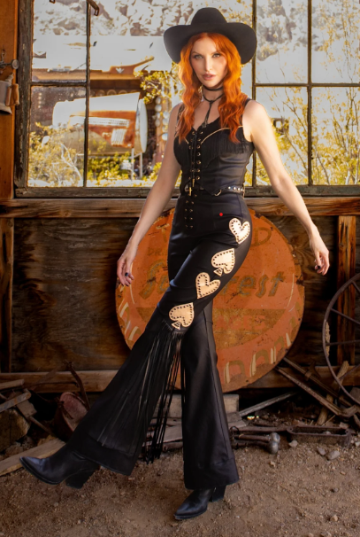 Woman in a black outfit with heart designs standing in a rustic setting.