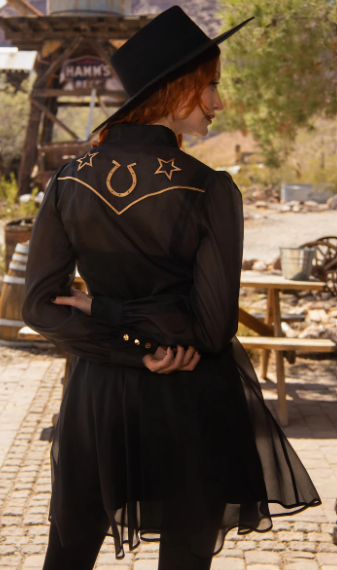 Person wearing a black cowboy hat and black shirt with gold embroidery in an outdoor setting.