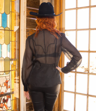 Person wearing a black sheer blouse and black hat in front of a stained glass window
