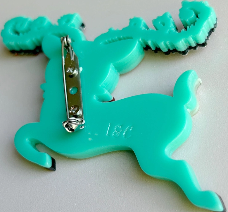 A turquoise plastic reindeer pinback brooch showing the back side with a silver metal safety pin clasp and '196' molded into the plastic, on a light gray background.
