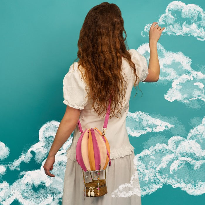 Woman in a white dress holding a colorful striped balloon against a teal background with cloud patterns.