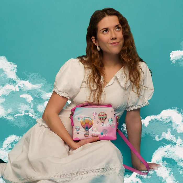 Woman holding a pink bag with hot air balloon design against a blue sky background