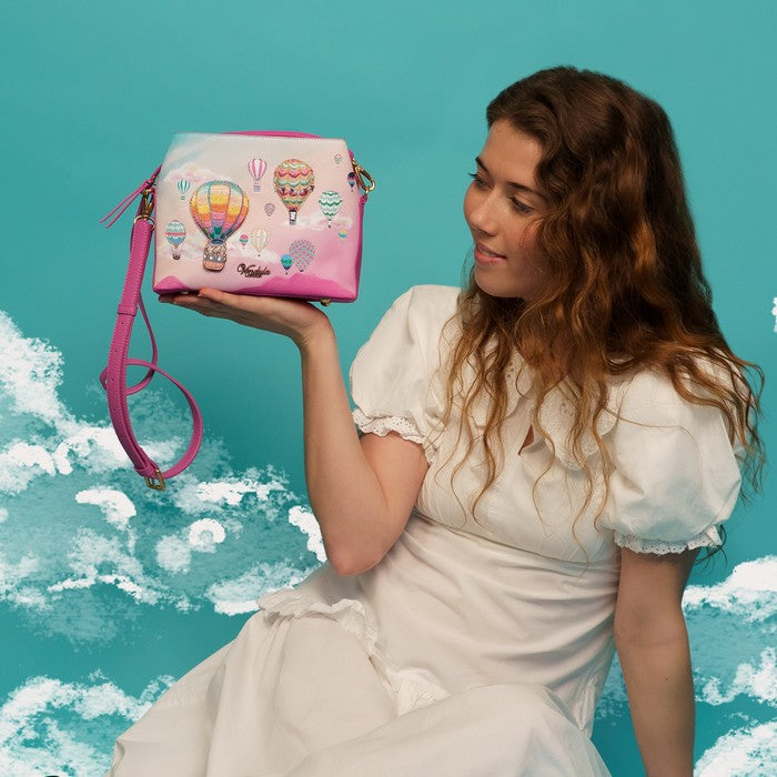 Woman holding a pink bag with hot air balloon designs against a blue sky background