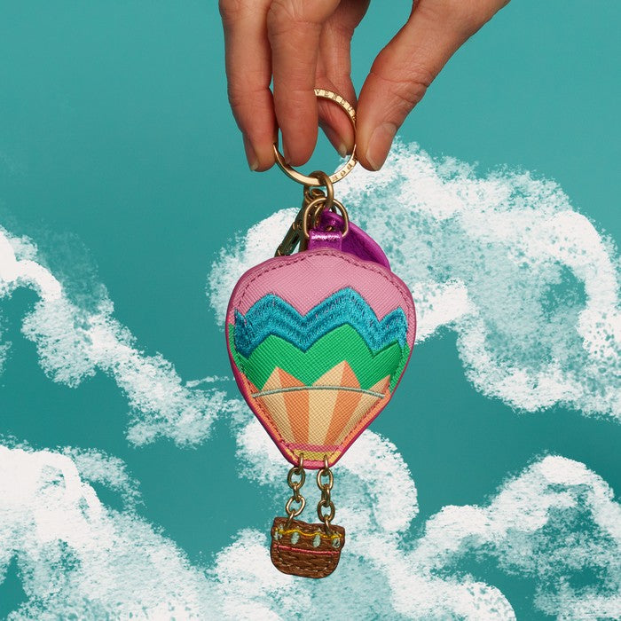 Colorful hot air balloon keychain held against a blue sky with white clouds.