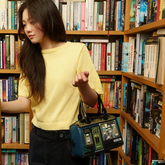 Woman in a yellow sweater holding a black bag with a vintage design in a bookstore.
