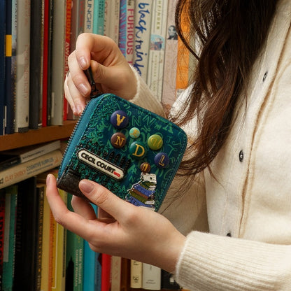 Person holding a blue wallet with decorative elements in front of a bookshelf