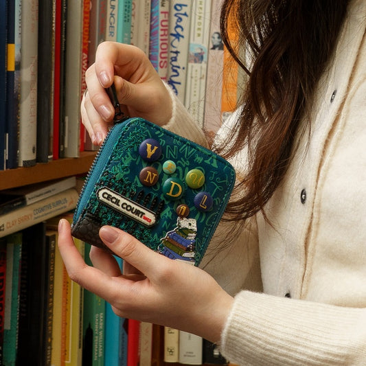 Person holding a blue wallet with decorative elements in front of a bookshelf