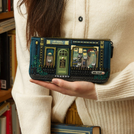 Person holding a decorative wallet with a book-themed design, surrounded by books.