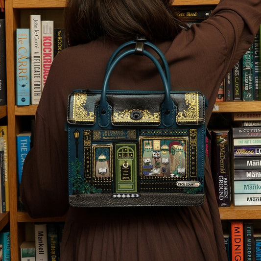 Person wearing a decorative handbag in front of a bookshelf