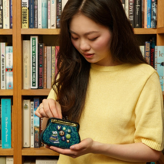 Woman holding a decorative blue purse in front of a bookshelf