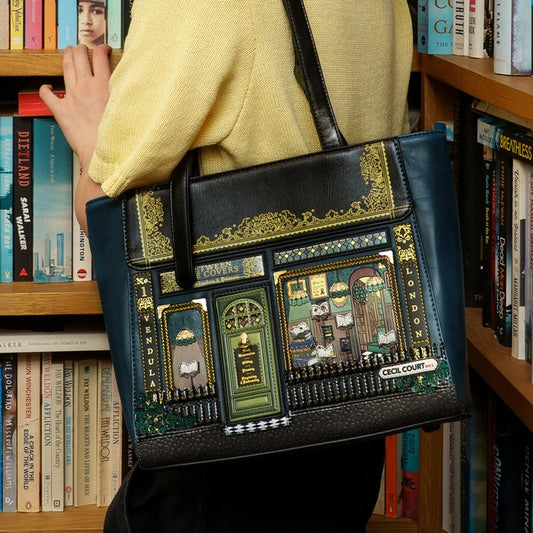 Person holding a black bag with decorative designs in front of a bookshelf