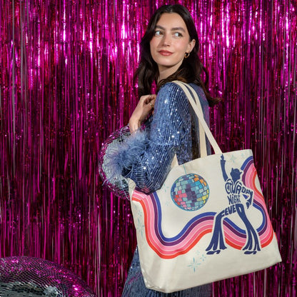 A woman wearing a sparkly blue sequined top carries a cream canvas tote bag with a colorful retro disco-themed graphic featuring a dancing figure, a disco ball, and the text 'Dancing Night Ever'. She is posed in front of a bright pink metallic tinsel curtain backdrop.