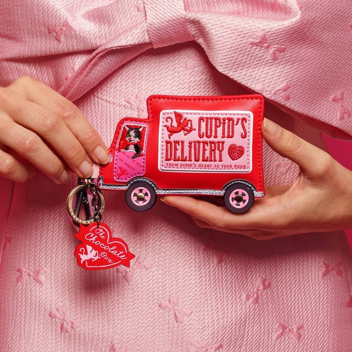 Red 'Cupid's Delivery' truck keychain held by hands on a pink textured background