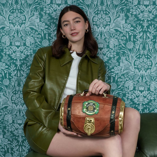Woman holding a barrel-shaped brown bag with intricate design against a patterned green wall.