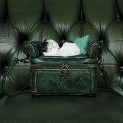 Green leather handbag with a cat inside on a green leather couch