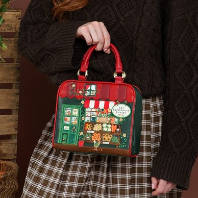 A person wearing a dark brown cable-knit sweater and a brown plaid skirt holds a small red and green handbag decorated with a detailed storefront illustration.