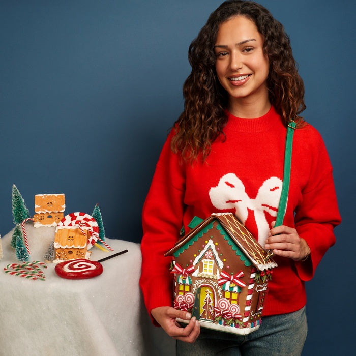 Woman in a red sweater holding a gingerbread house with decorative elements on a blue background