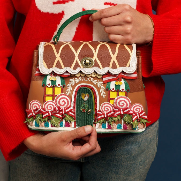 Gingerbread house-shaped handbag held by a person wearing a red sweater.