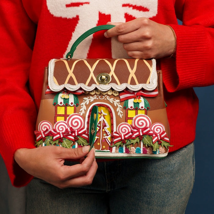 Gingerbread house-shaped handbag held by a person wearing a red sweater.