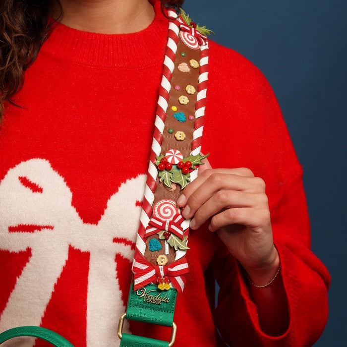 Person wearing a red sweater holding a decorative strap with candy cane design against a blue background