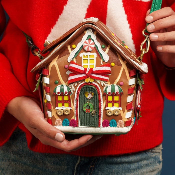 Gingerbread house-shaped handbag held by a person wearing a red sweater.