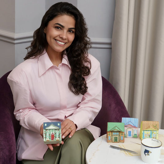 Woman holding a small decorative box with more boxes and a mug on a table in front of her.