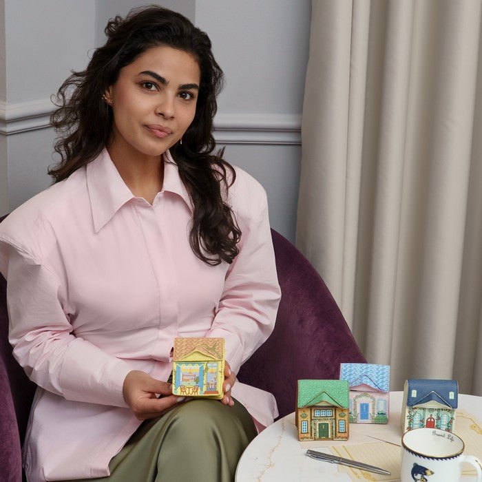 Woman holding a small house model with more house models on a table in front of her.