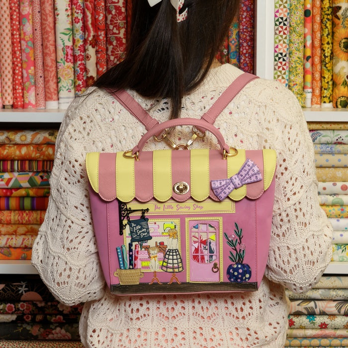 Person wearing a pink and yellow backpack with a store design, in front of fabric rolls.