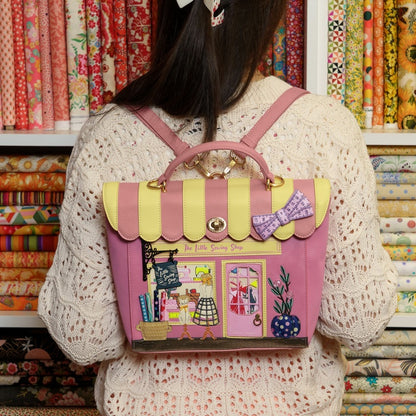 Person wearing a pink and yellow backpack with a store design, in front of fabric rolls.