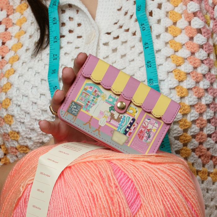 Person holding a colorful knitted item with a small bag featuring a store design.