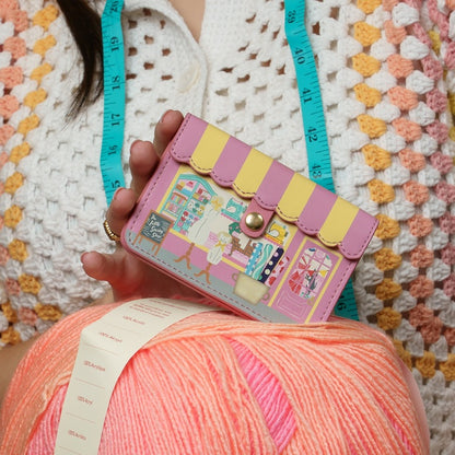 Person holding a colorful knitted item with a small bag featuring a store design.