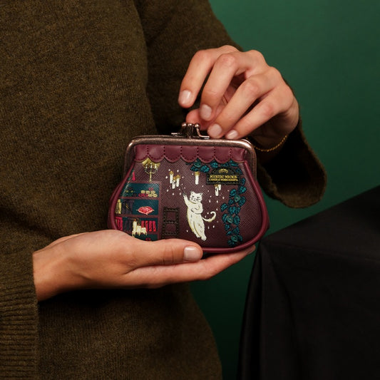 Person holding a small embroidered purse with a cat design against a green background