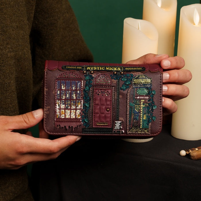Person holding a decorative wallet with intricate designs in front of lit candles.