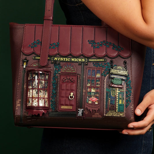 Handbag designed like a small town with 'Mystic Wicks' sign, held by a person.