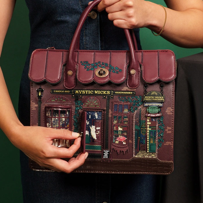 Person holding a decorative handbag with 'Mystic Nicks' design against a green background