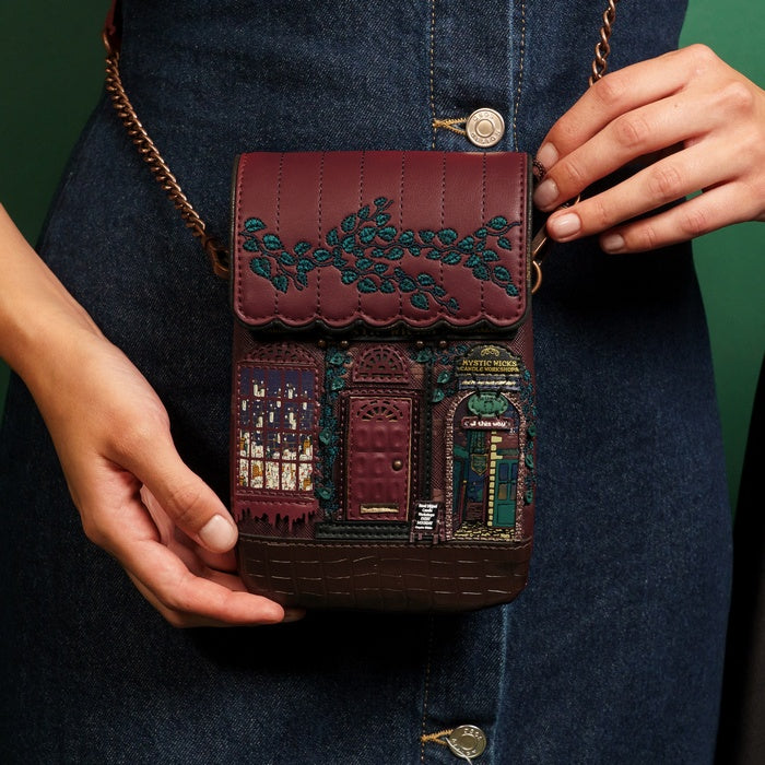 Person holding a maroon handbag with decorative designs on a dark background