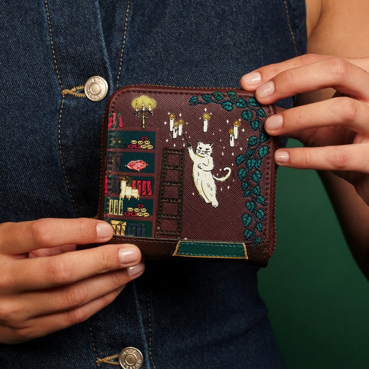 Person holding a embroidered wallet with cat designs against a denim background