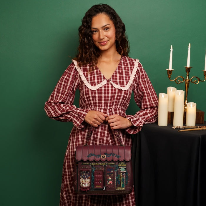 Woman in a red plaid dress holding a matching bag with candles and a candelabra in the background.