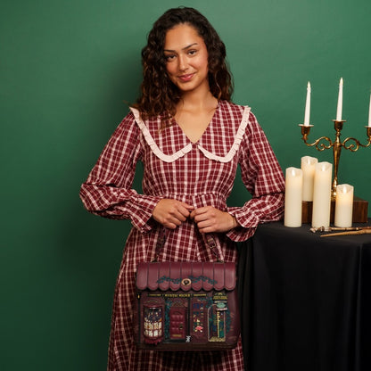 Woman in a red plaid dress holding a matching bag with candles and a candelabra in the background.
