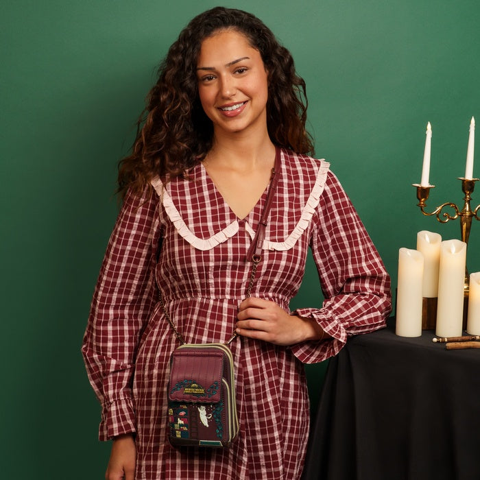 Woman in a red plaid dress with a small bag, standing next to a table with candles against a green background