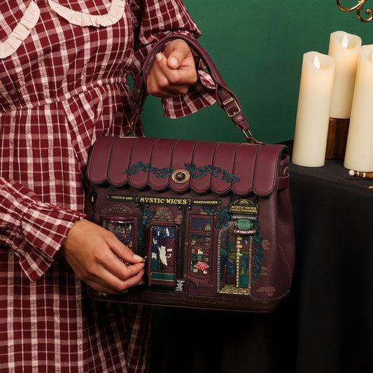 Person holding a detailed handbag with a building design, against a green background with candles.