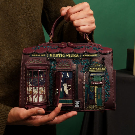 Person holding a decorative handbag with intricate designs and text, against a green background.