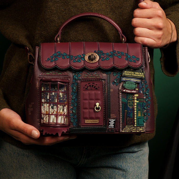 Handbag with decorative design held by a person against a dark background
