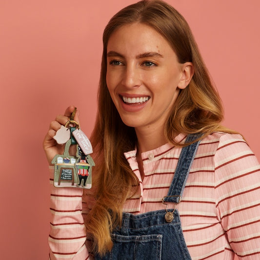 Woman holding a keychain with a house and figures against a pink background