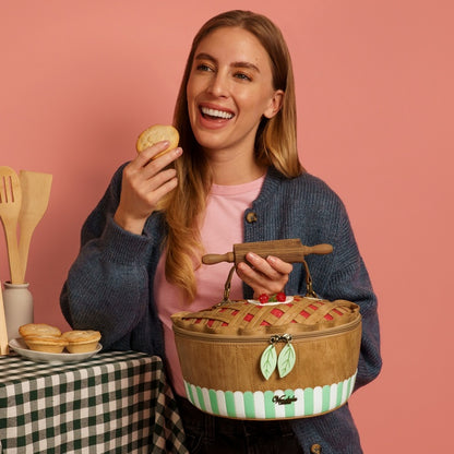 Woman holding a pie and a picnic basket against a pink background