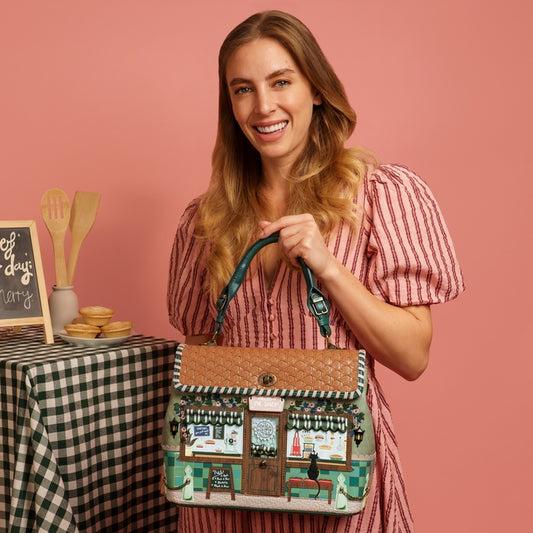 Woman holding a decorative bag with a vintage café design against a pink background