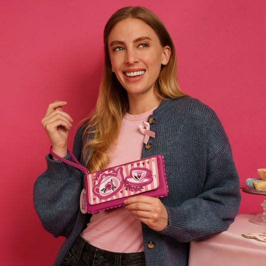 Woman holding a pink wallet with a cat design against a pink background