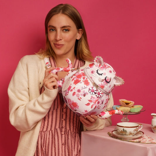Woman holding a floral teapot with a pink background