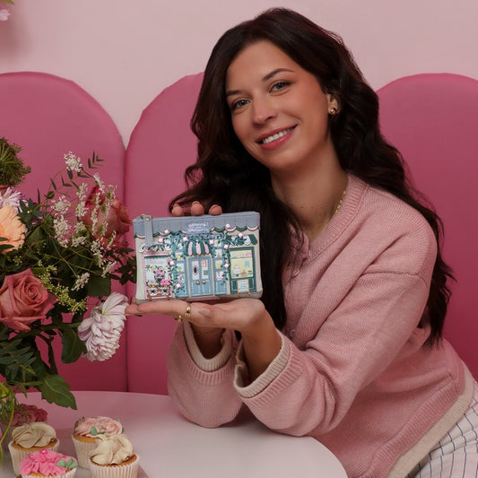 Woman holding a small travel-sized makeup case with a pink background and floral decorations.