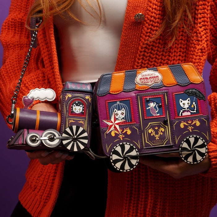 Person holding a colorful handbag with decorative elements against a purple background